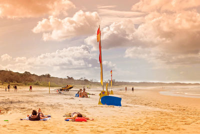 People enjoying at beach against cloudy sky