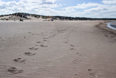 Footprints on sand at beach against sky