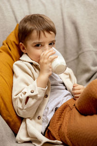 Little adorable boy sitting on the couch at home and drinking milk. fresh milk in glass