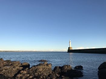 Lighthouse by sea against clear blue sky