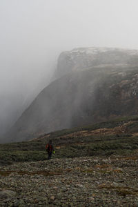 Rear view of man standing on mountain against sky during foggy weather