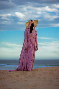 Front view of a muslim girl wearing a veil and hijab standing on beach sand against the cloudy sky