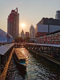 Bridge over river by buildings against sky during sunset