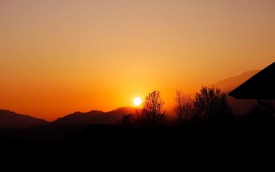 Silhouette trees on landscape against orange sky