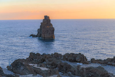 Rock formation in sea against sky during sunset