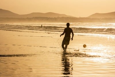 Silhouette man with ball on beach against sky during sunset