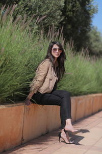 Portrait of beautiful young woman sitting on retaining wall