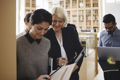 Smiling female lawyers discussing while walking with coworkers in library