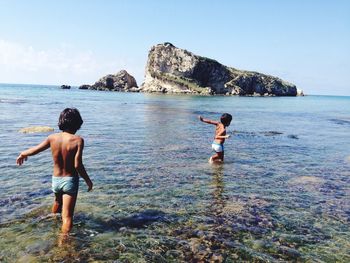 Rear view of shirtless boy in sea against sky