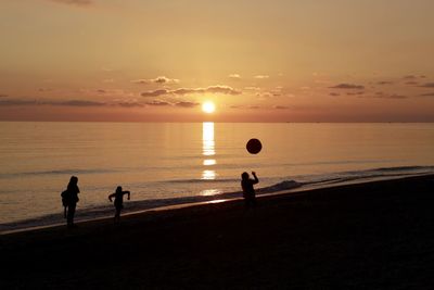 Silhouette people playing on beach against sky during sunset