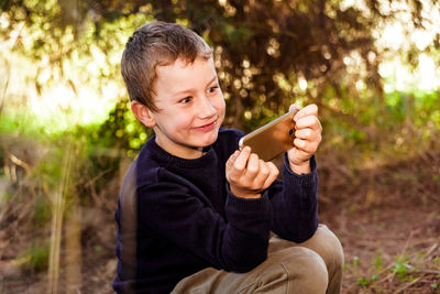 Smiling boy holding mobile phone while sitting outdoors