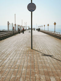 Street lights on footpath by sea against clear sky