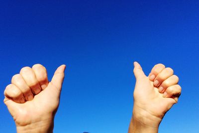 Cropped hands gesturing thumbs up against clear blue sky