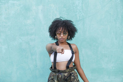 Portrait of woman with curly hair wearing sunglasses standing against wall