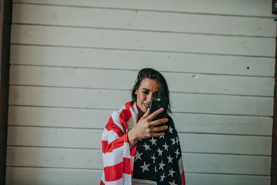 Woman wearing american flag using phone against wall