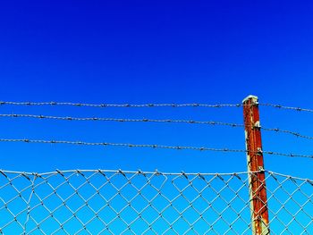 Low angle view of fence against blue sky