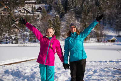 Portrait of happy woman by daughter with arms raised in snow during winter