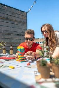 Concentrated young man pushing jenga game piece next to female friend in rooftop party