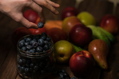 Cropped hand holding blueberries in jar on table