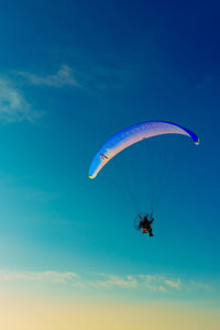 Low angle view of person paragliding against blue sky