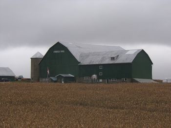 Barn on field by buildings against sky