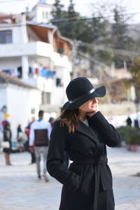 Young woman wearing hat standing against city in background