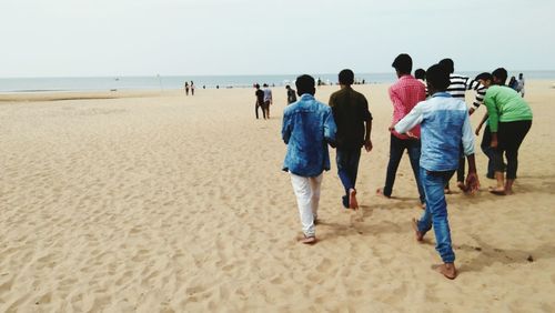 People walking on shore at beach against sky