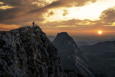 Man with bike on top of mountain at sunset