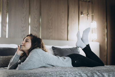 Young woman using mobile phone while sitting on bed at home