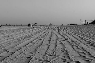 Tire tracks on sand dunes against clear sky