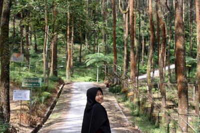 Portrait of young woman standing amidst trees in forest