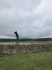 Side view of person walking on retaining wall against cloudy sky