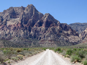 Dirt road by mountain against sky