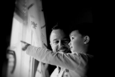 Happy father with son pointing outside window at home