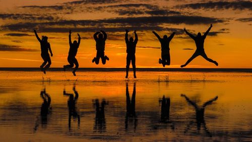 Silhouette friends jumping over reflection at salar de uyuni during sunset