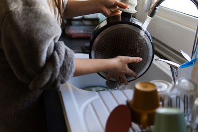 Unrecognizable woman washing pot at the kitchen sink dressed in winter robe