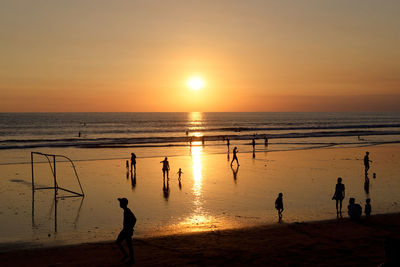 Silhouette people on beach against sky during sunset