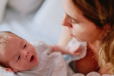 From above closeup of loving mother holding adorable newborn baby while sitting on bed at home