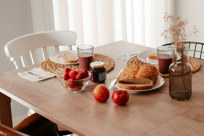 Slices of fresh bread served on table with ripe red strawberries and apples near glasses with beverages in light kitchen