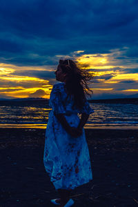 Woman standing at beach against sky during sunset