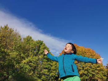 Boy standing by plants against blue sky