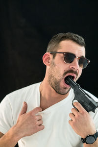 Man pointing gun in mouth against black background