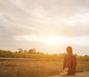 Rear view of man sitting on field against sky