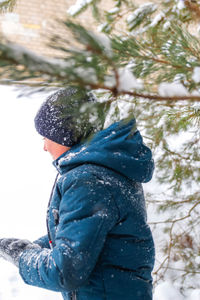  smiling child boy in winter forest in snowstorm. smiling kid standing near tree on snowy background. 