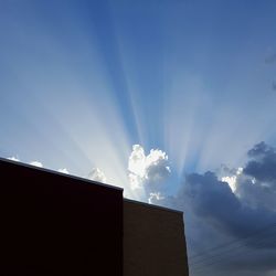 Low angle view of sunlight streaming through building against sky