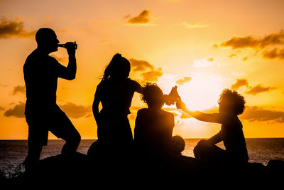 Friends toasting with bottles, beautiful sunset. people enjoying together, cheering with drinks 