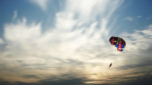 Low angle view of people paragliding against sky during sunset