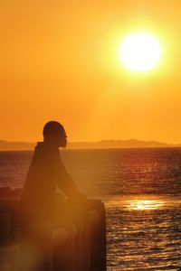 Man sitting against sea during sunset