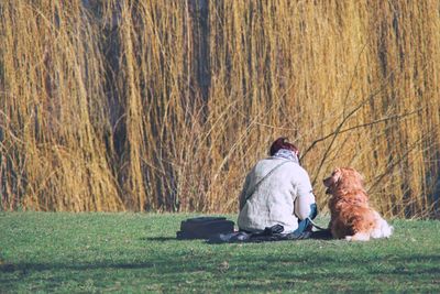 Rear view of woman and dog sitting on field