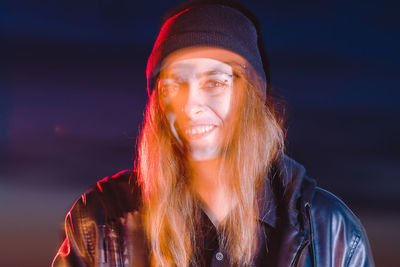 Double exposure portrait of young woman standing against black background, smiling 